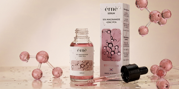 Érnè serum 10% Niacinamide + Zinc PCA w szklanej butelce z różowym płynem, pudełku, na mokrym tle z molekułami.