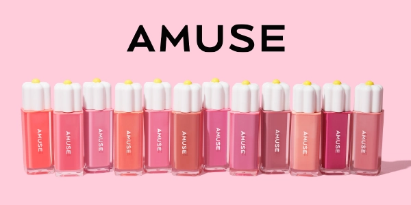 AMUSE błyszczyki do ust w rzędzie, z białymi nakrętkami przypominającymi stokrotki, na różowym tle.