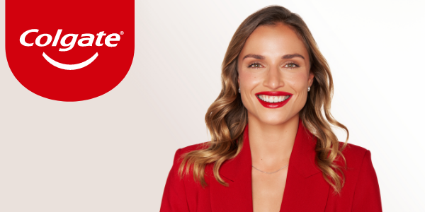 Logo Colgate obok uśmiechniętej kobiety w czerwonym żakiecie, prezentującej białe zęby.
