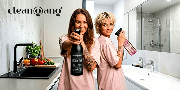 Dwie uśmiechnięte kobiety trzymają spraye czyszczące clean@gang: czarny "BLACK AS F*ST" i różowy, w łazience i kuchni.
