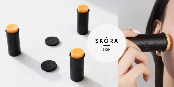 Skóra Skin stick balms: black tubes with orange product, one applied to a face, two shown upright.