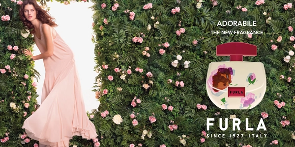 Furla Adorabile new fragrance bottle with floral art; woman in pink dress among green foliage and pink roses.