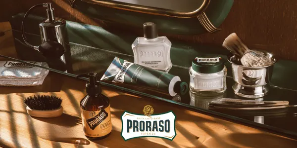 Elegancki zestaw Proraso: kremy, balsam, pędzel, brzytwa na drewnianej toaletce w ciepłym świetle.