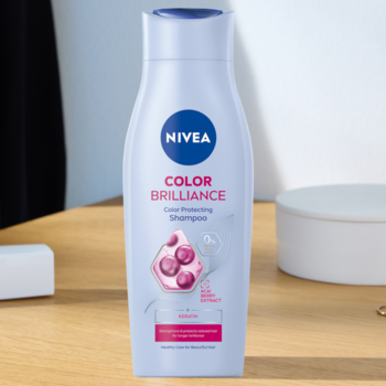 Fioletowy szampon NIVEA Color Brilliance do włosów farbowanych, butelka w kształcie klepsydry na stole.