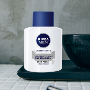 Balsam po goleniu NIVEA MEN Silver Protect, biała butelka z niebieską nakrętką na ciemnej tacy.