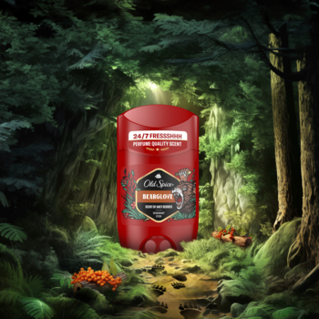 Czerwony sztyft Old Spice Bearglove dezodorant, z etykietą z niedźwiedziem, na tle ciemnego, zielonego lasu.