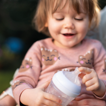 Uśmiechnięte dziecko trzyma butelkę Philips Avent Natural z responsywnym smoczkiem do łączenia karmień.