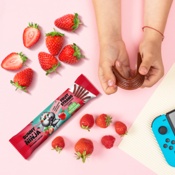Widok z góry: czerwona przekąska owocowa Bunny & Ninja (pałeczki jabłko-truskawka) z truskawkami i dłońmi dziecka.