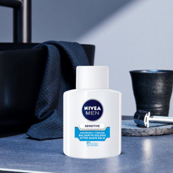 Balsam po goleniu NIVEA MEN Sensitive Cooling w białej butelce z niebieskim napisem, na tle łazienki z umywalką i maszynką.