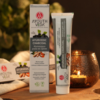 AYOUTH VEDA Ayurvedic Charcoal wybielająca pasta do zębów z węglem, tubka i pudełko na tle ze świecą.