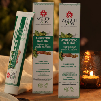 AYOUTH VEDA Ayurvedic Natural, wybielająca pasta z imbirem i miętą, tubka i dwa pudełka, ciepłe tło ze świecą.