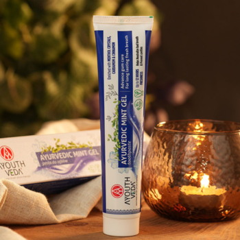 AYOUTH VEDA Ayurvedic Mint Gel, biała tubka z niebieskimi pasami, widok z przodu. Tło z pudełkiem i świecą.