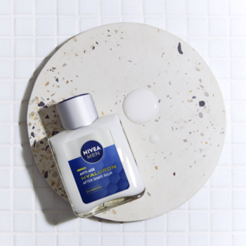 Balsam NIVEA MEN Anti-Age Hyaluron w białej butelce, widok z góry na beżowej podstawce terrazzo z kroplą.