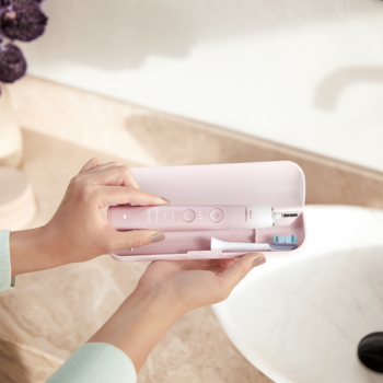 Ręce trzymają otwarte różowe etui podróżne ze szczoteczką elektryczną Philips Sonicare DiamondClean w łazience.