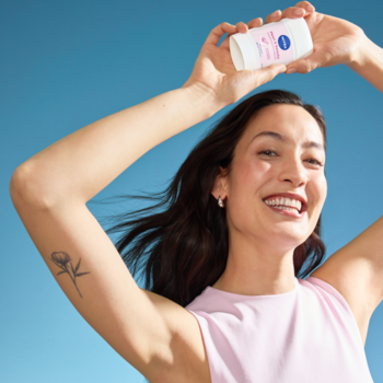 Kobieta uśmiecha się, trzymając różowo-biały antyperspirant NIVEA w sztyfcie pod błękitnym niebem.