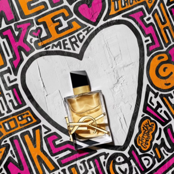 Woda perfumowana YSL Libre w butelce z logo YSL i złotym płynem, widok z góry na tle białego serca graffiti.