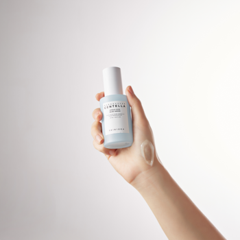Ręka trzyma jasnoniebieskie serum Skin1004 Hyalu-Cica Blue z białą nakrętką; kropla na skórze.