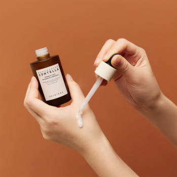 Madagascar Centella Probio-CICA Intensive Ampoule. Dłoń aplikuje białe serum z brązowej butelki z kroplomierzem.