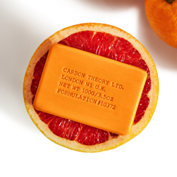 Carbon Theory Vitamin C Cleansing Bar, pomarańczowa kostka w przekrojonym czerwonym grejpfrucie, zbliżenie z góry.