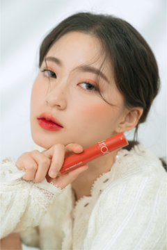 Kobieta trzyma błyszczyk Rom&nd Juicy Lasting Tint nr 07, czerwoną pomadkę z intensywnym połyskiem na ustach.
