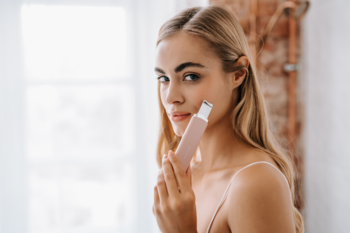 Kobieta z blond włosami trzyma różowe urządzenie do peelingu kawitacyjnego B-Scrub PRO Slim przy twarzy, oczyszczając skórę.