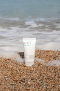 Biała tubka Zero Sun Clean 01 Fresh, kremu przeciwsłonecznego SPF 50+, stoi na mokrym piasku przy falach oceanu.