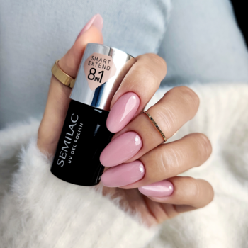 Ręka z różowymi, błyszczącymi paznokciami, trzymająca czarny lakier hybrydowy Semilac Smart Extend 8.1, widok z bliska.