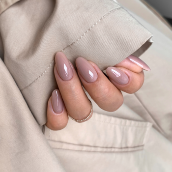 Zbliżenie na dłoń z migdałowymi paznokciami pomalowanymi beżowym lakierem hybrydowym Semilac 815 o wysokim połysku.