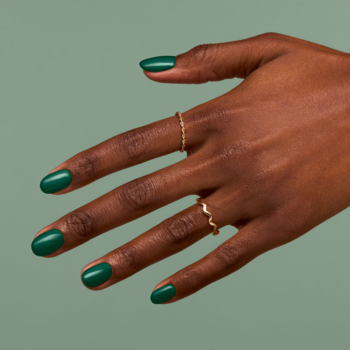 Dłoń z lakierem hybrydowym Semilac 309 Pine Green, głęboka ciemna zieleń, złote pierścionki, na jasnym tle.