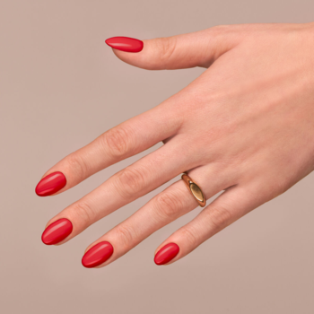 Zbliżenie na kobiecą dłoń z gładkimi, czerwonymi paznokciami Semilac Spiced Apple; na palcu złoty pierścionek.