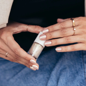 Dłonie trzymają brokatowy lakier Semilac, z paznokciami pomalowanymi lśniącym, perłowym odcieniem syrenki.