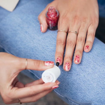 Zbliżenie na dłonie malujące paznokcie czerwonym, brokatowym lakierem Semilac o błyszczącym wykończeniu.