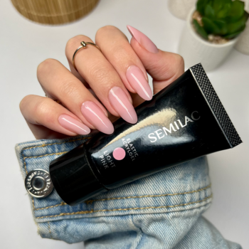 Dłoń z półtransparentnymi, jasnoróżowymi paznokciami trzyma akrylożel Semilac, tuba z logo na pierwszym planie.