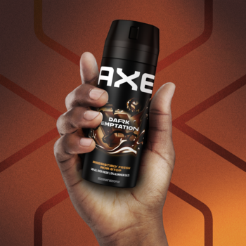 Dezodorant Axe Dark Temptation w czarnej puszce z czekoladowymi akcentami, trzymany dłonią na wzorzystym tle.