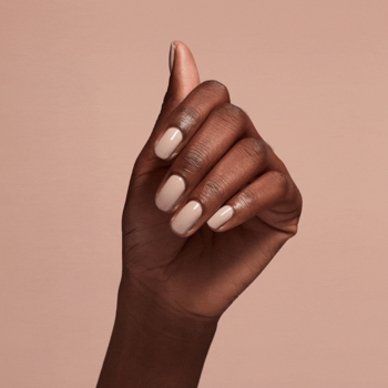 Zbliżenie na dłoń z ciemną karnacją i paznokciami pokrytymi cielistą odżywką OPI Nail Envy Nude-y.