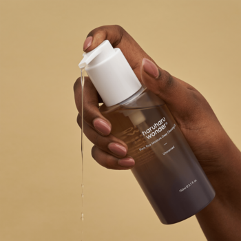 Haruharu Wonder Black Rice olejek do demakijażu, ciemna butelka z pompką, dłoń wyciska olejek, zbliżenie.