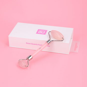 Ilū roller z różowego kwarcu do masażu twarzy z dwoma końcówkami, w otwartym białym pudełku, z boku.