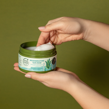 Dłonie nabierają kremową maskę Petal Fresh z algami i arganem z zielonego słoika, na oliwkowym tle.