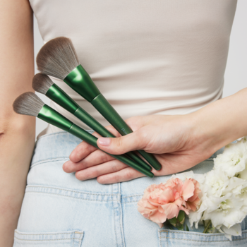 Trzy pędzle Donegal Blooming Bliss z zielonymi rączkami, wegańskie. Trzymane za plecami w jeansach z kwiatami.