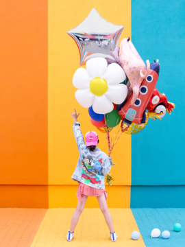 Biały balon foliowy PartyDeco stokrotka z żółtym środkiem, na przyjęcia, trzymany przez osobę od tyłu.