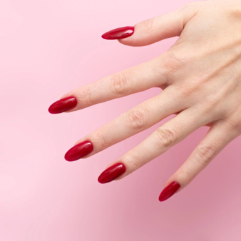Dłoń z czerwonymi, migdałowymi paznokciami pokrytymi lakierem hybrydowym Semilac Radiant Raspberry na różowym tle.