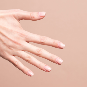 Zbliżenie na kobiecą dłoń z naturalnymi paznokciami, prezentującymi efekt bazy hybrydowej Semilac Skin Tone Cover Base nude.