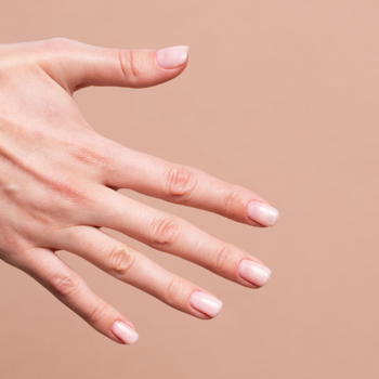 Dłoń z subtelnym manicure Semilac Skin Tone, mleczny róż z połyskującym pyłkiem na beżowym tle.