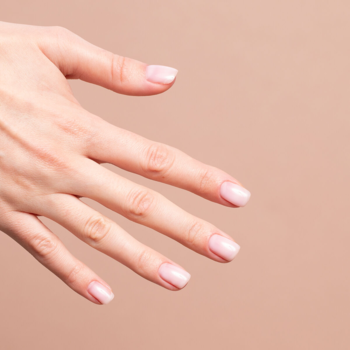 Zadbana dłoń z naturalnymi paznokciami pomalowanymi bazą Semilac Skin Tone Cover Base mleczny róż, na tle nude.