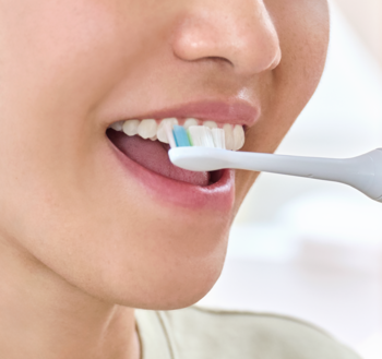 Osoba szczotkująca zęby elektryczną szczoteczką Philips Sonicare W2 Optimal White, widok na niebiesko-zielone włókna.