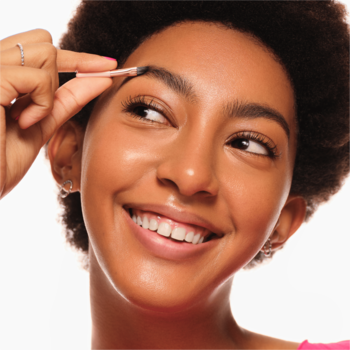 Młoda kobieta z uśmiechem stylizuje brwi pędzelkiem z Essence Brow Powder Duo Dark na białym tle.