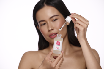 Kobieta trzyma Hada Labo Hyalu Renew rewitalizującą esencję. Przejrzysta butelka z olejkową formułą i kroplomierzem.