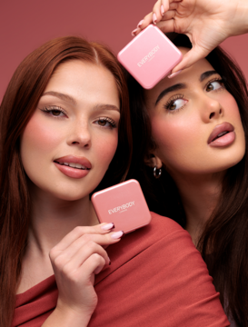 Dwie modelki z różem rozświetlającym Everybody London Pink w różowych kompaktach, podkreślający promienną cerę.