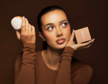 Modelka prezentuje puder wygładzający Everybody London x Sosfa w kompakcie i pędzel do makijażu na brązowym tle.