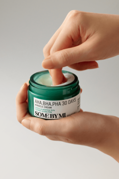 Krem Some By Mi AHA BHA PHA Miracle Cream w zielonym słoiku, dłoń zanurza palec. Złuszczający krem do cery trądzikowej.